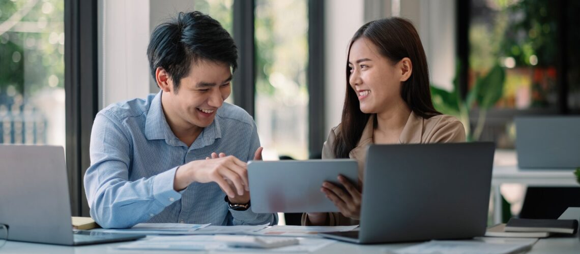 Two business professionals demonstrating emotional intelligence leadership through collaborative discussion with technology in modern workspace