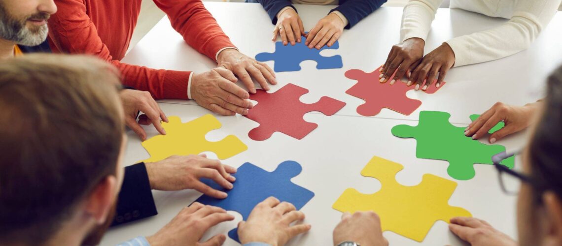 Business team collaborating to connect red, yellow, green and blue puzzle pieces representing Insights Discovery colour energies working together