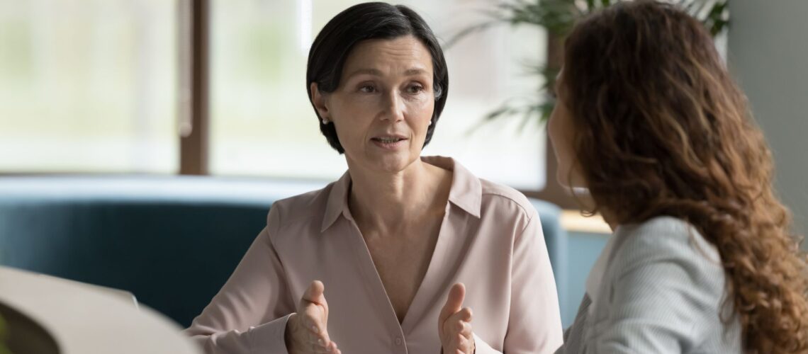 Experienced leadership coach facilitating development conversation with professional in modern office setting
