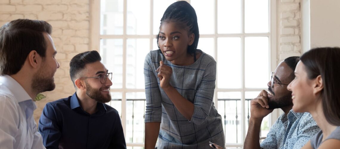 Confident female leader facilitating collaborative team meeting with diverse professionals in modern office