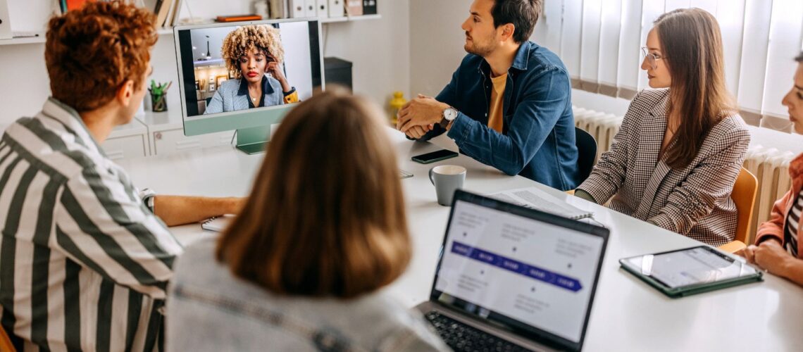 Professional hybrid team meeting with colleagues joining by video conference in modern office