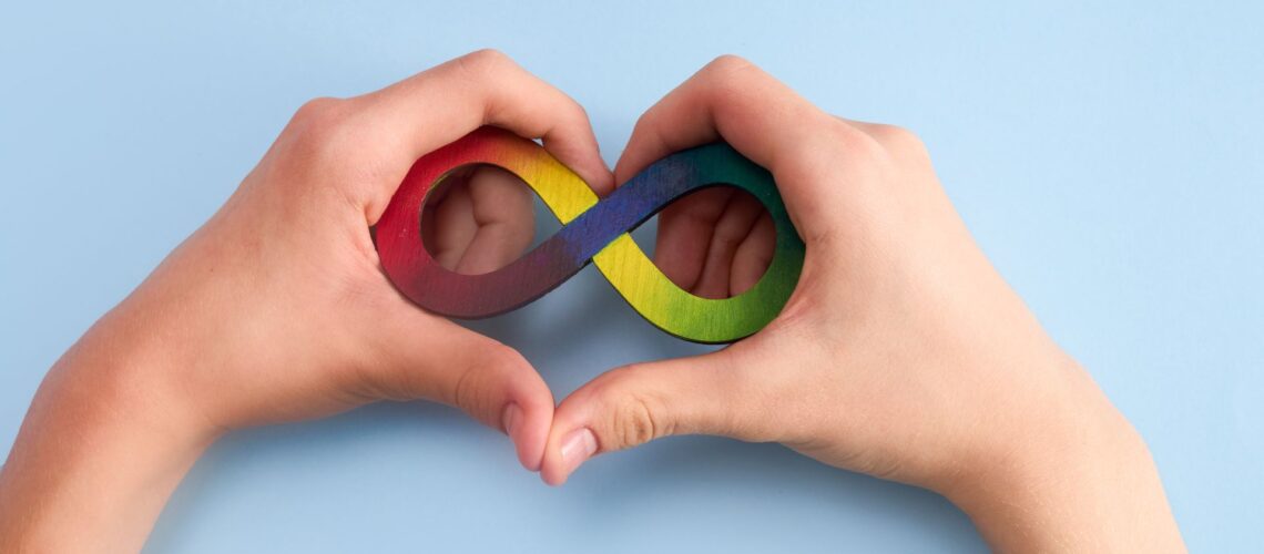 Hands forming heart shape around colourful neurodiversity infinity symbol representing workplace inclusion and support