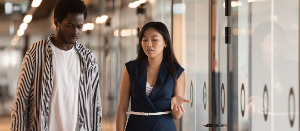 Two diverse professionals having an engaging discussion in modern office corridor, demonstrating inclusive workplace communication
