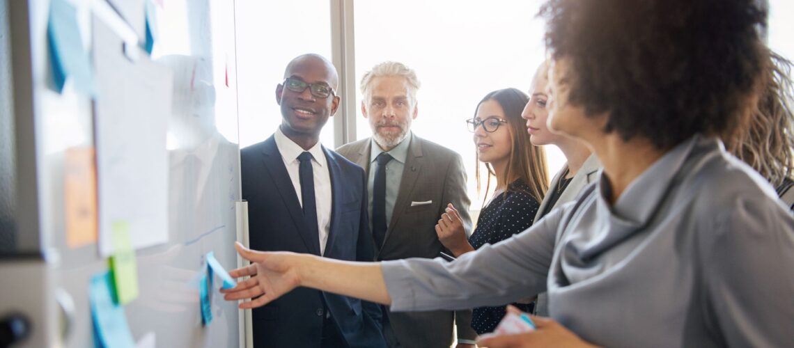 Female leader facilitating strategic discussion with diverse team at whiteboard during organizational change workshop