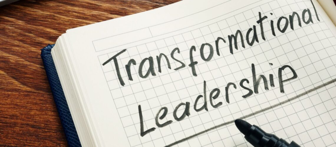 Notebook with "Transformational Leadership" handwritten on grid paper next to black marker on wooden desk