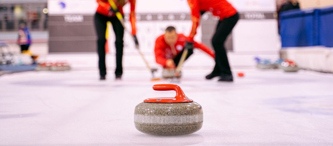 Curling stone in focus with team sweeping behind, symbolising team resilience under pressure