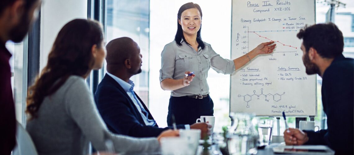 A pharmaceutical professional presenting clinical trial results confidently to a small team in a bright modern meeting room