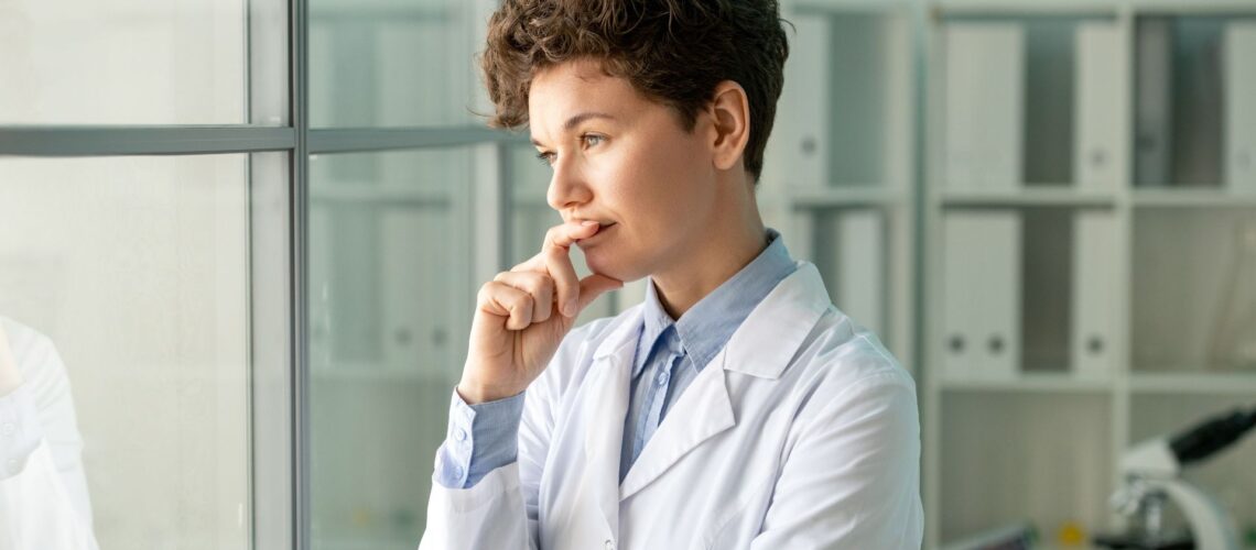 Scientist in a lab coat pausing thoughtfully by a window, reflecting on leadership values